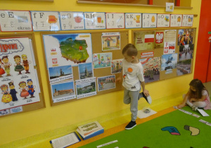 Chłopiec stoi pod tablicą i wskazuje jedną z ilustracji, opowiada co na niej widać.